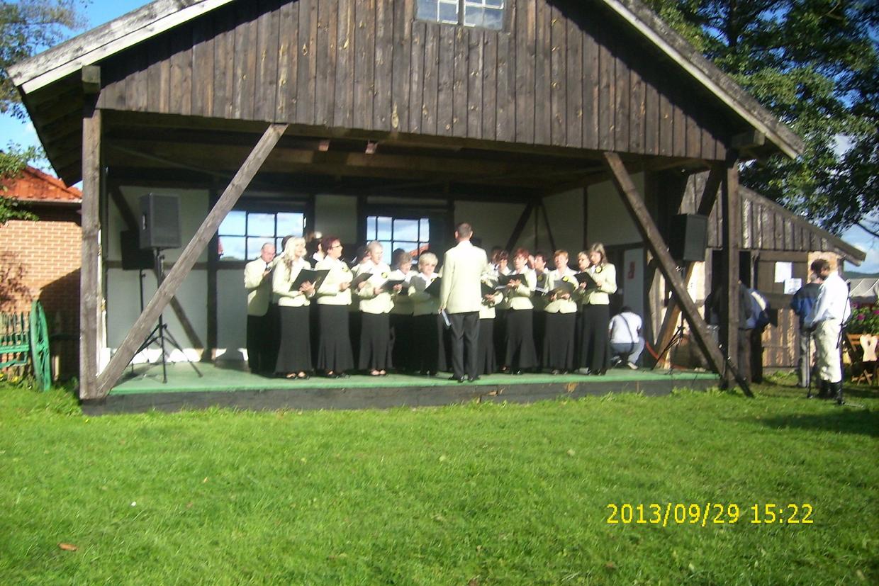 Chór śpiewa na drewnianej scenie w skansenie kaszubskim w Nadolu.