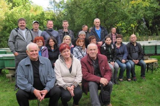 Grupa uczestników Dni Pszczelarzy pozuje na tle zieleni i pasieki.