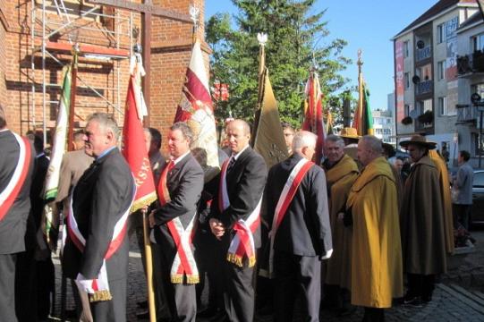 Pszczelarze w galowych strojach z flagami i ceremonialnych szatach idą w pochodzie.