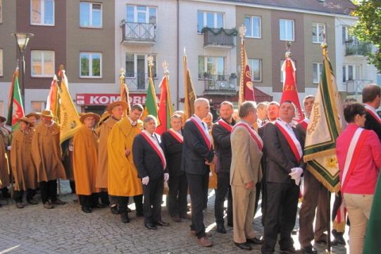 Zgromadzenie pszczelarzy z Koszalina w uroczystych strojach niosących sztandary.