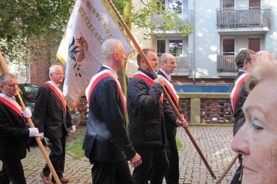 Mężczyźni z flagą stowarzyszenia pszczelarzy maszerują na obchodach w Koszalinie.