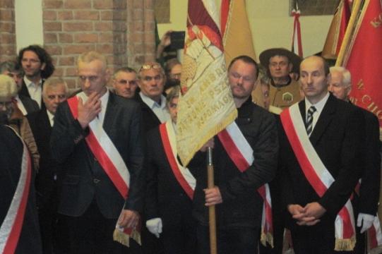 Mężczyźni w garniturach z szarfami i flagami podczas Dni Pszczelarzy w Koszalinie.