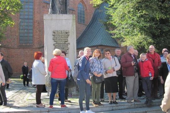Pszczelarze i goście Ogólnopolskich Dni Pszczelarzy przy pomniku i historycznym budynku.