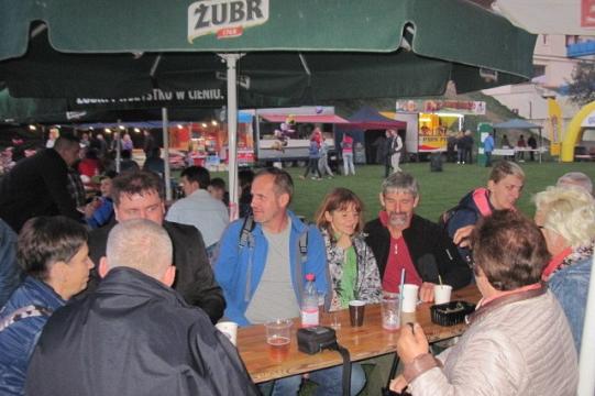 Ludzie siedzą przy stolikach pod zielonymi parasolami podczas Dni Pszczelarzy Koszalin 2017.