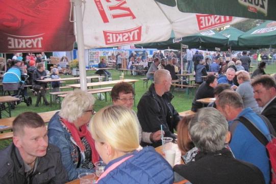 Goście Dni Pszczelarzy w Koszalinie siedzą pod parasolami i rozmawiają.
