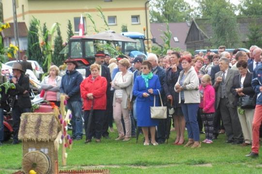 Uczestnicy obchodów 35-lecia Koła Pszczelarzy stoją na trawie przy pamiątkowej rzeźbie.