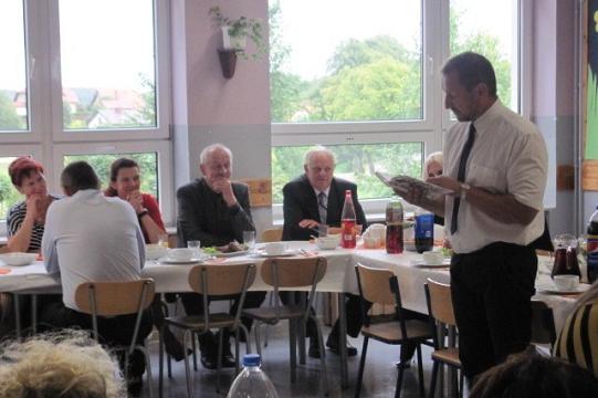 Mężczyzna przemawia na jubileuszu Koła Pszczelarzy, inni siedzą przy stole.