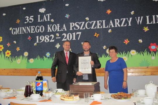 Trzy osoby z dyplomem na tle transparentu 35-lecia Koła Pszczelarzy.