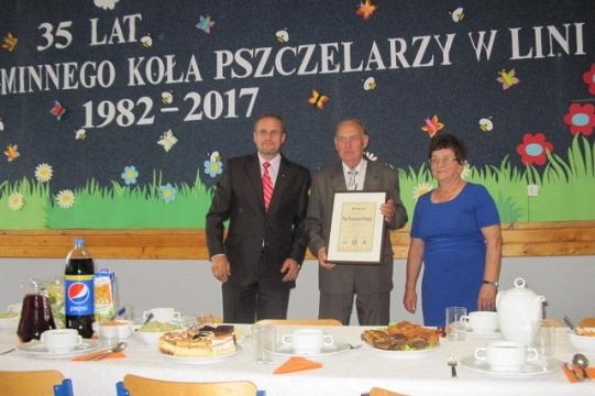 Pszczelarze celebrują 35-lecie Koła w Lini, z dyplomem na tle okolicznościowego baneru.