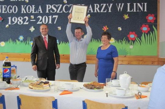 Uroczystość 35-lecia Koła Pszczelarzy, z osobą środkową dumnie wznoszącą wręczony dyplom.