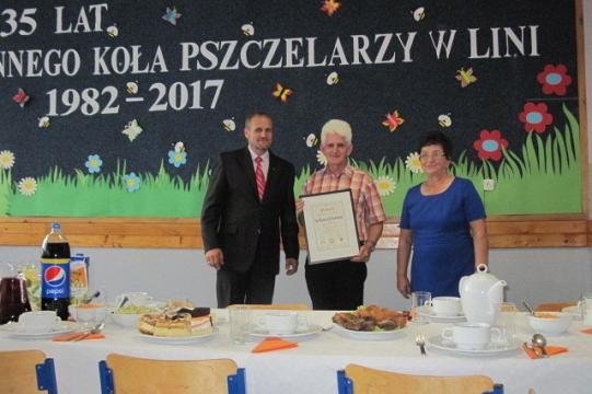 Trzy osoby na tle baneru 35-lecia Koła Pszczelarzy, kobieta odbiera dyplom.