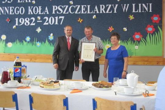 Trzy osoby z dyplomem na tle baneru 35-lecia Koła Pszczelarzy w Linii.