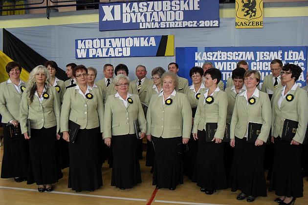 Członkowie chóru Pięciolinia w jasnych strojach pozują na tle planszy.