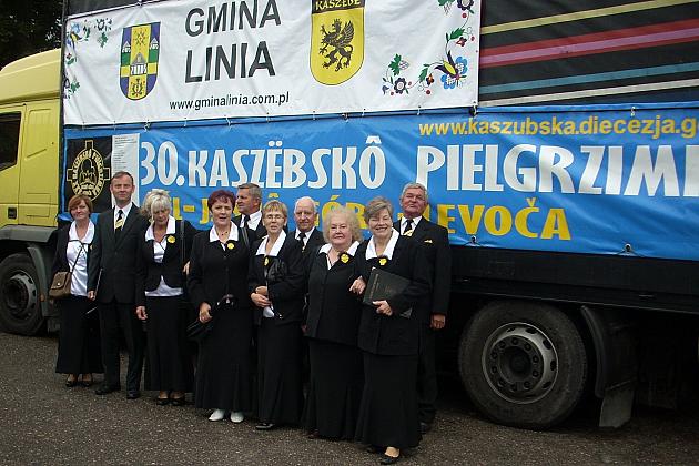 Chór Pięciolinia z Gminy Linia w strojach chórowych stoi przed pojazdem z banerami.