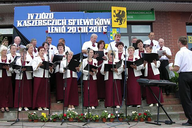Chór Pięciolinia w ludowych strojach śpiewa pod batutą dyrygenta na plenerowej scenie.