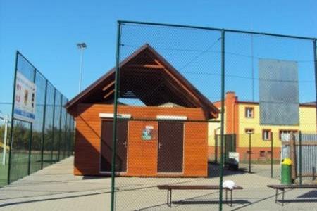 Pawilon sportowy Orlik 2012 z ogrodzeniem i ławką na tle nieba.