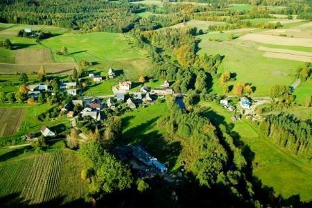 Lotnicza panorama zielonej wsi w Gminie Linia, z domami, polami i wijącą się rzeką.