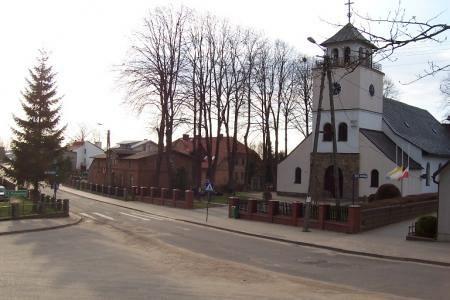 Biały kościół z wieżą przy drodze w Lini otoczony nagimi drzewami.