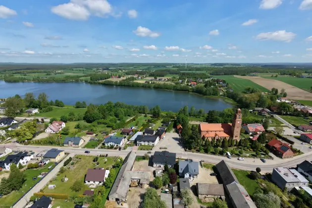 Lotnicza panorama gminy Linia z jeziorem, zabudową mieszkalną i kościołem.
