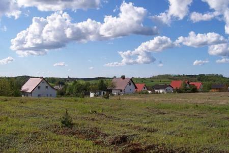Widok na Miłoszewo z polami, zabudowaniami i błękitnym niebem z chmurami.