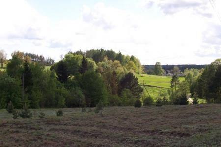 Zaorane pole, zielone drzewa, pagórki i jasne niebo w wiejskim plenerze.