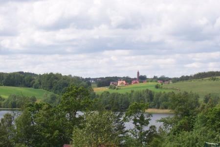 Malowniczy widok na pagórki Miłoszewa, zieleń drzew i budynek na horyzoncie.