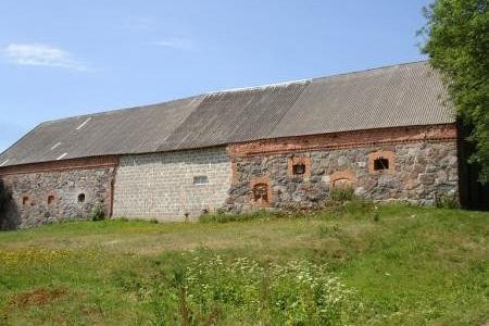 Kamienna stodoła w Pobłociu z szarym dachem na tle błękitnego nieba.