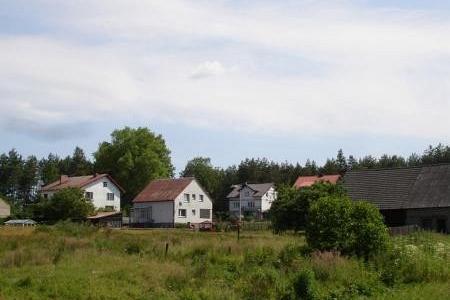 Pobłocie: kilka domów otoczonych zielonymi polami i drzewami pod chmurami.