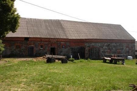 Dawna wiejska stodoła z kamienia i drewna na zielonym trawniku Pobłocia.