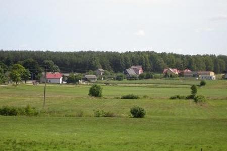Zielone pola z balotami siana, domy i las na horyzoncie, typowy widok Pobłocia.