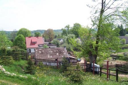 Stary budynek wśród bujnej zieleni, z innymi domami w tle, tworzący wiejski krajobraz Potęgowa.