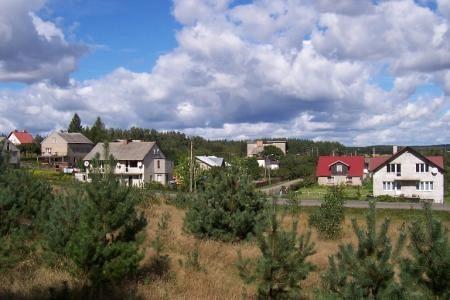 Panoramę Strzepcza z domami, zielenią i niebem pełnym chmur.