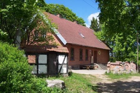 Stary drewniany budynek z czerwonym dachem otoczony zielenią w Strzepczu Głodnicy.