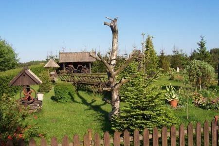 Wiejski ogród z tradycyjnym domem, rzeźbionym słupem i zielenią, typowy dla Głodnicy.