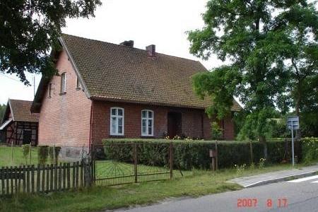 Ceglany dom w Tłuczewie wśród zieleni przy drodze.