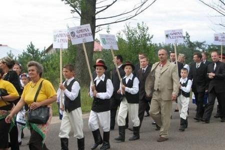 Uczestnicy Dożynek Powiatowo-Gminnych 2007 w strojach ludowych maszerują z tablicami.