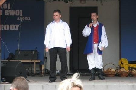 Scena z dożynek: dwóch mężczyzn, jeden w stroju ludowym, drugi w białej koszuli.