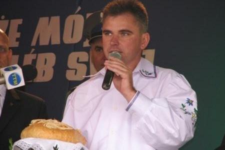 Mężczyzna z mikrofonem i dożynkowym chlebem na stole.