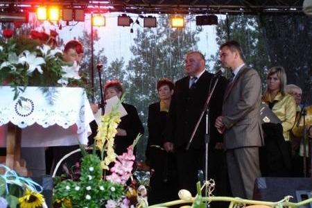 Uczestnicy dożynek gminnych na scenie, mężczyzna przemawia do publiczności.