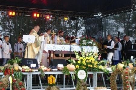 Msza dożynkowa celebrowana przez księdza przy ołtarzu, z dekoracjami kwiatowymi i zbożowymi.