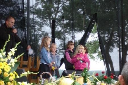 Rodziny z dziećmi celebrujące Dożynki Gminne 2008 przy stole z kwiatami.