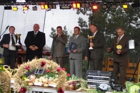 Mężczyźni na scenie podczas Dożynek Gminnych 2008, przed nimi wieniec dożynkowy.