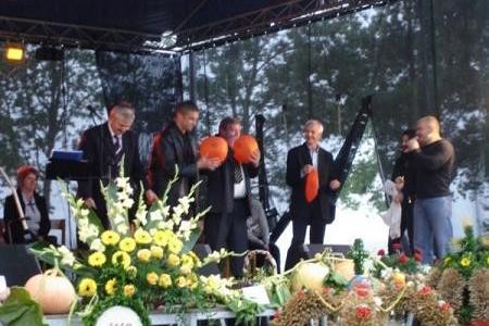 Uczestnicy dożynek gminnych przemawiają na scenie wśród kwiatowych dekoracji.