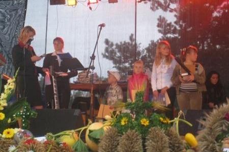 Uczestnicy dożynek na scenie otoczeni plonami i dekoracjami.