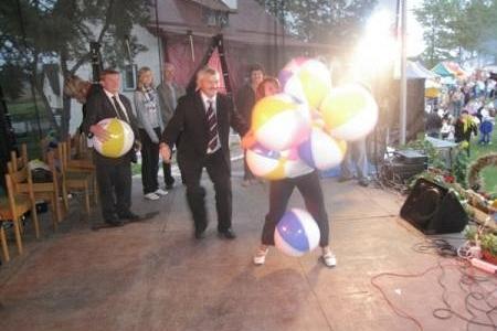 Osoby na dożynkach gminnych, kobieta w centrum z pękiem jasnych balonów.