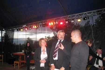 Uczestnicy Dożynek Gminnych 2008 pozują na tle oświetlonej sceny, mężczyzna z mikrofonem.