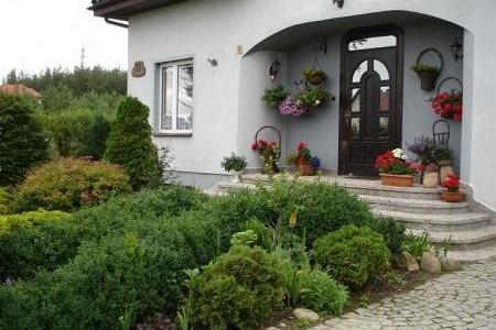 Wiejski dom z pięknie zagospodarowanym ogrodem i ukwieconym wejściem.