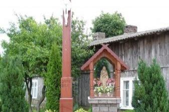 Krzyż i kapliczka przydrożna w wiejskim krajobrazie.