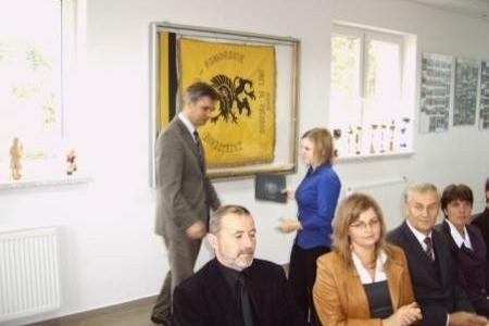 Wręczenie stypendium studentce przez mężczyznę w obecności innych osób.
