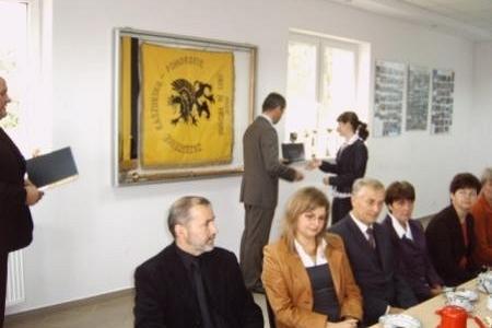 Mężczyzna wręcza studentce stypendium, inni uczestnicy uroczystości siedzą przy stole.